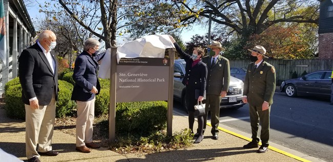Two park employees work with three people in formal wear to unveil the Park Service sign.