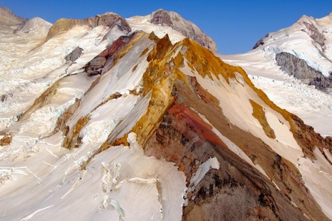 Iliamna Volcano covered in snow and colorful rocks.