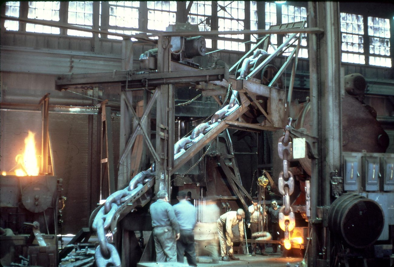 workers in the chain forge constructing giant chains as it moves up and along a pulley system