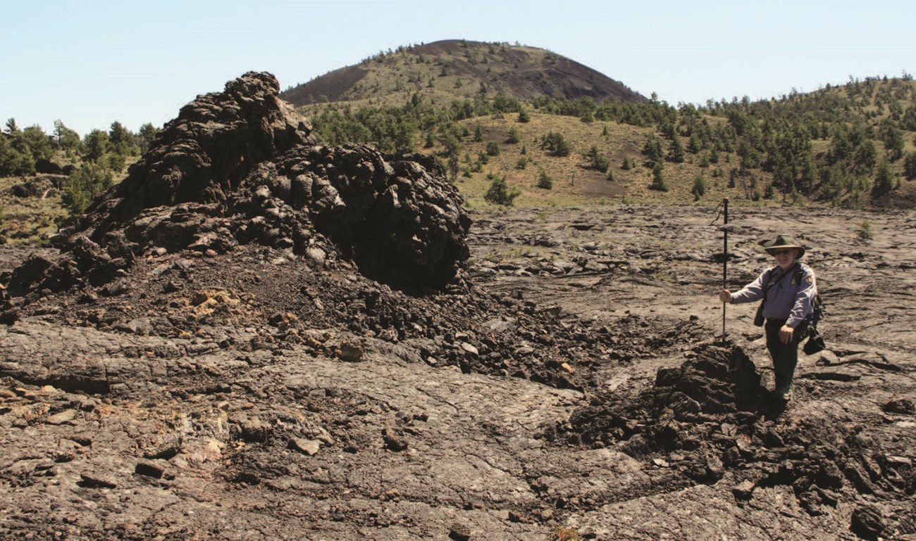 photo of a person standing on lava rock near taller points of rock