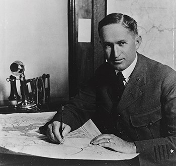 Yellowstone Superintendent Horace M. Albright wearing a three piece suit sits at a desk while holding a pen.