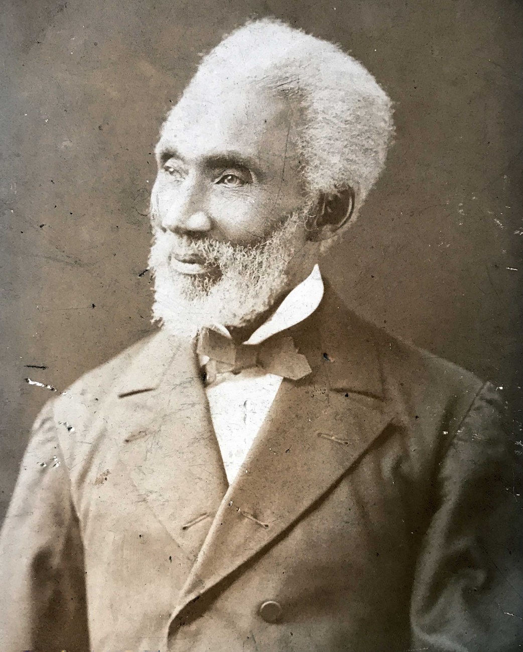 Photographic portrait of Reverend William Jackson in formal attire, late 1800s. Bust-length photographic portrait of a grey or white-haired Black man with a beard looking towards his right, wearing a dark suit, light shirt, and a dark-colored bow tie.