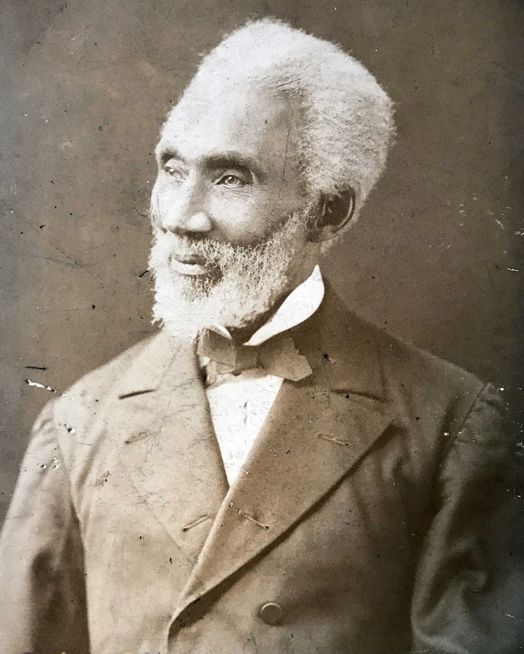 Photographic portrait of Reverend William Jackson in formal attire, late 1800s. Bust-length photographic portrait of a grey or white-haired Black man with a beard looking towards his right, wearing a dark suit, light shirt, and a dark-colored bow tie.