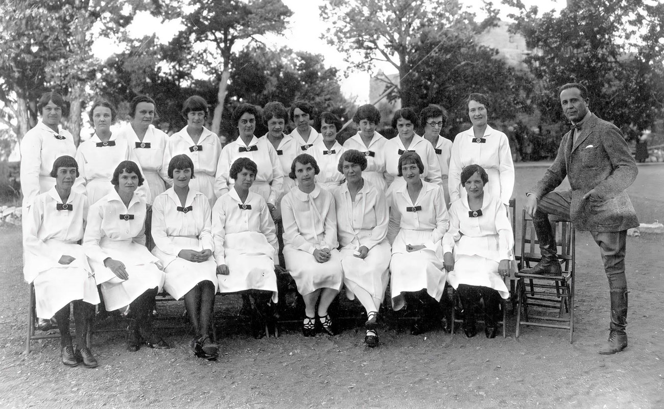 El Tovar Hotel's Harvey Girls at Grand Canyon Circa 1926. Fred Harvey General Manager Victor Patrosso, right, posing with group of 20 El Tovar Harvey Girls arranged in two rows, in in all white evening uniforms.