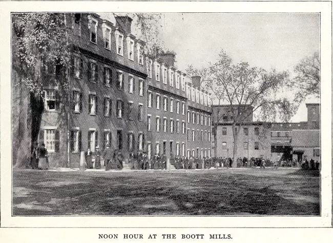 1890s-late-1900s-Noon-Hour-at-Boott-Mills-Boardinghouses-John-French-St Text reads "Noon hour at the Boott Mills." A line of women file out of a mill toward a boardinghouse