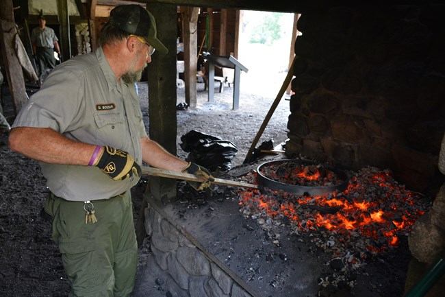 uniformed park ranger with metal rod poking hot coals in a forge.