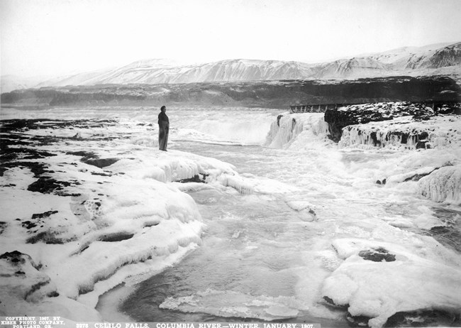 Waterfall in winter with ice interspersing water. Man stands in foreground.