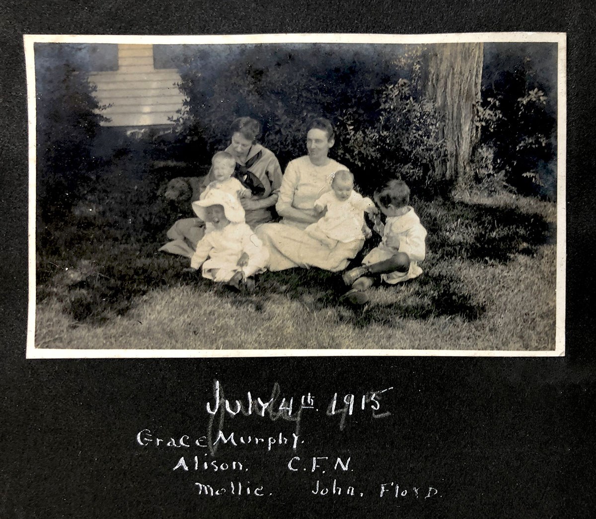 A black and white photograph depicts two women sitting with a group of children.