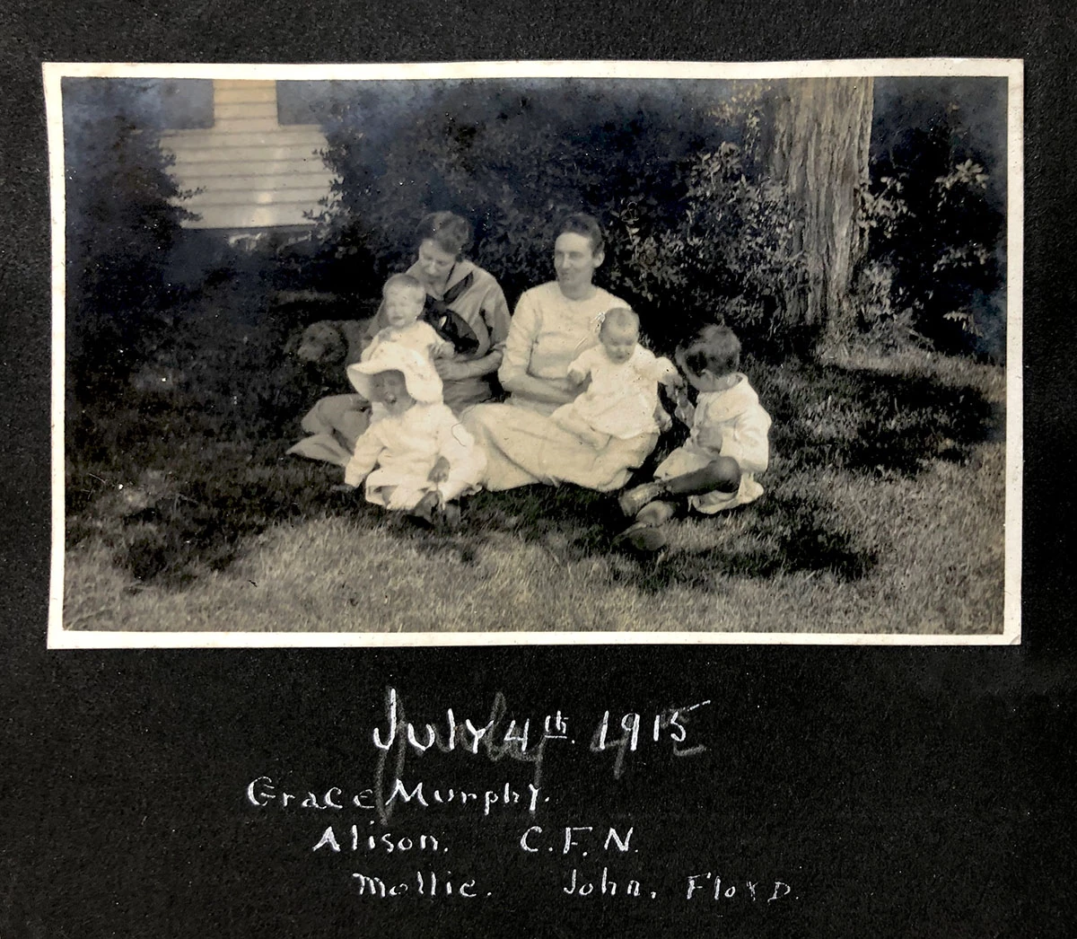 Fourth of July 1915. A black and white photograph depicts two women sitting with a group of children.