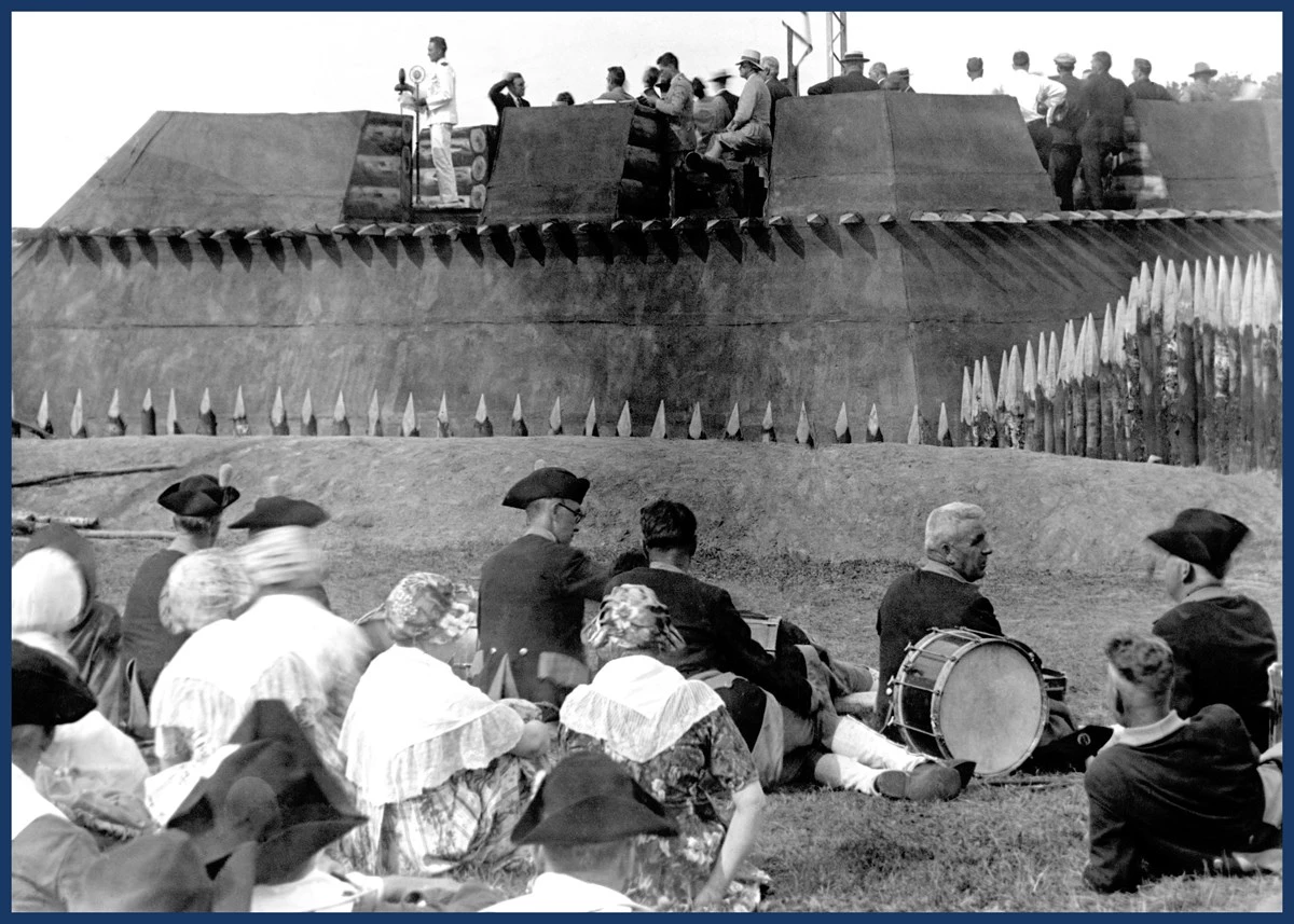 1927BirdAddress A man in a crisp white uniform stands in a miniature wooden fort addressing a crowd.