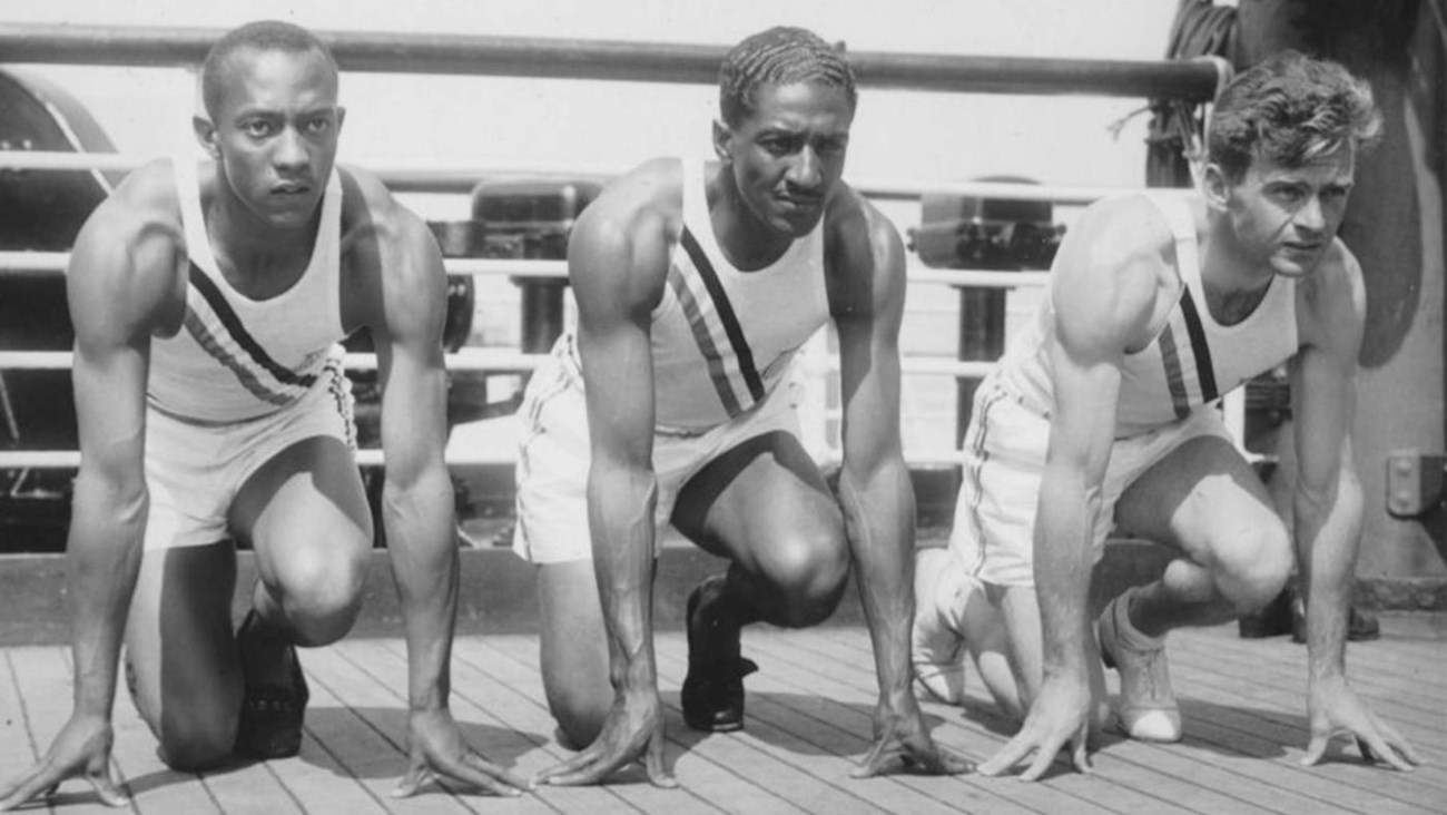 1936 Olympics Jesse Owens, Ralph Metcalfe, and Frank Wykoff on SS Manhattain public domain Three Olympic athletes crouched down, prepared to have a foot race.