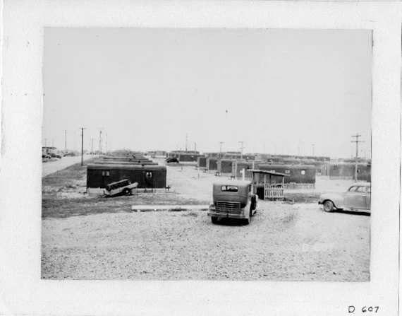 1940s cars in black and white before rows of single story temporary housing extending into distance.