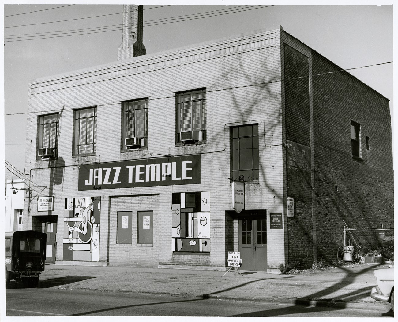 Street view of the "Jazz Temple,” a brick cube-shaped building with abstract murals on the front.