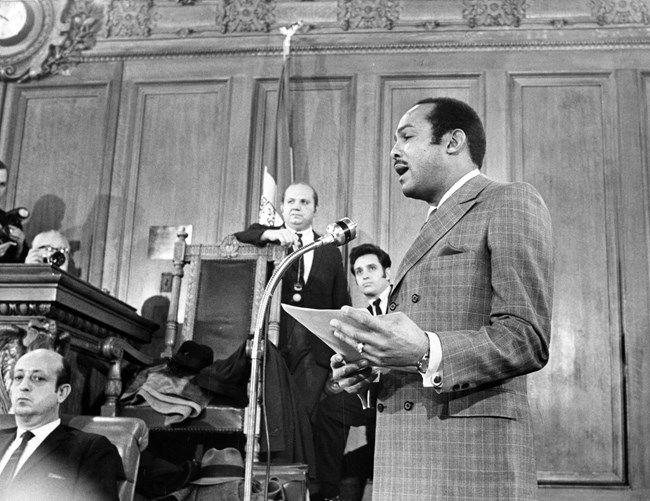 A man at a podium talks to a room of people.