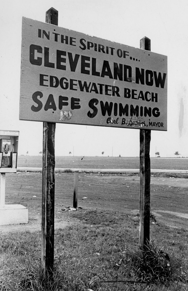 Sign reads “In the Spirit of Cleveland Now Edgewater Beach Safe Swimming. Carl B Stokes, Mayor.”