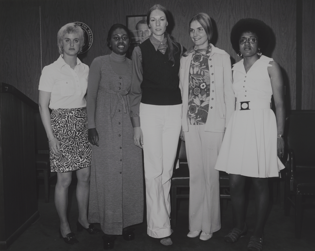 Three white and two Black women wearing civilian clothes stand in a line posing for the photo.