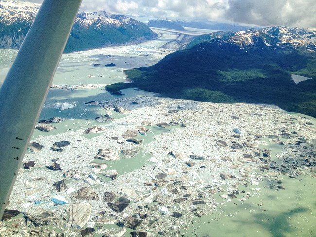 view of Alsek lake from a plane. Icebergs choke the pale glacier-fed lake.