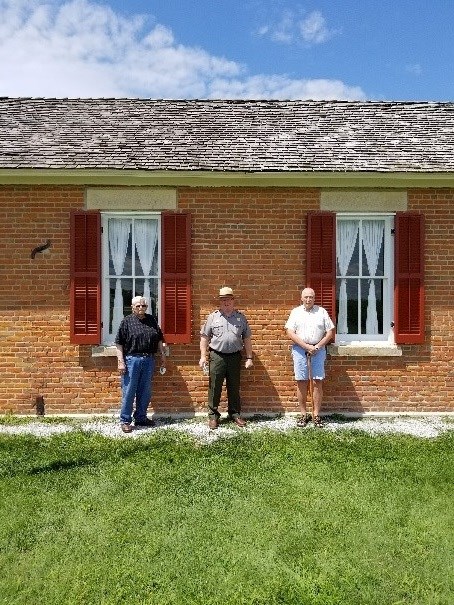 A ranger and two visitors stand outside the brick one-room school.