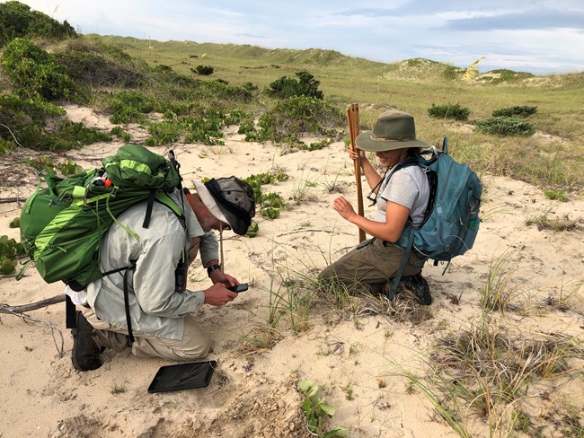 two people with backpacks kneeling in the sand