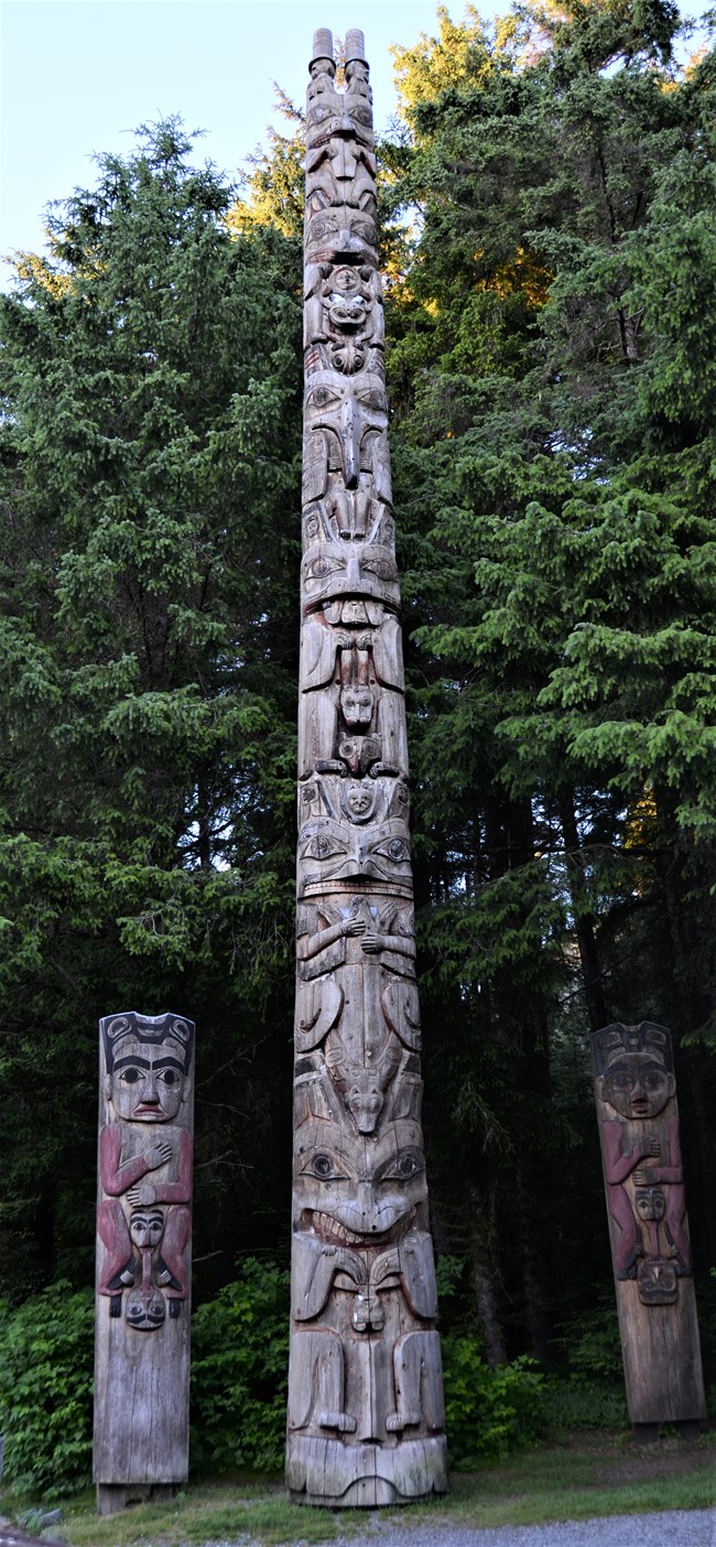 A tall totem pole and two house posts at the entrance of a trail