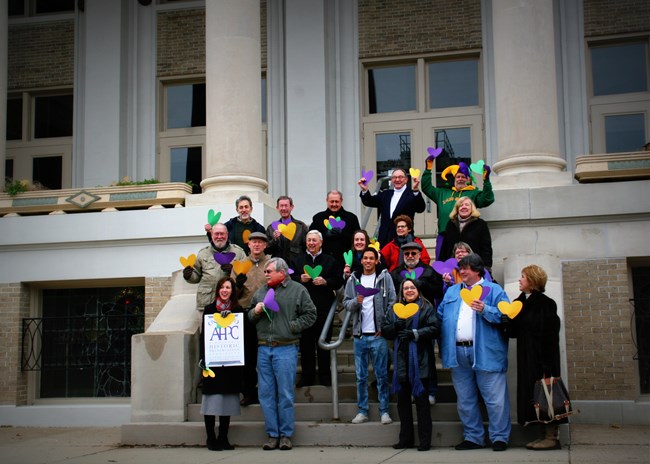 About a dozen Garden District Neighborhood Foundation Members standing in front of building.