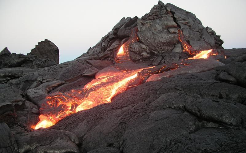 20030621-0700_DAS_large Photo of a dome shaped lava with dark rock forming a crust and molten lava leaking out from cracks at its base.