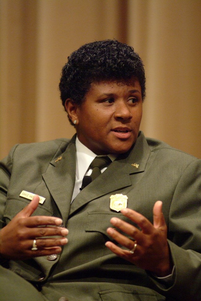 A seated African American woman in a formal green ranger uniform speaks and gestures with her hands.