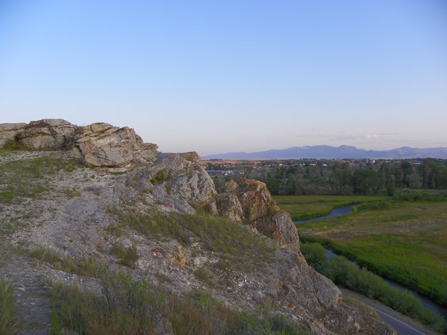 Photograph of a large rocky outcrop with a long distance view of agricultural land and town buildings.