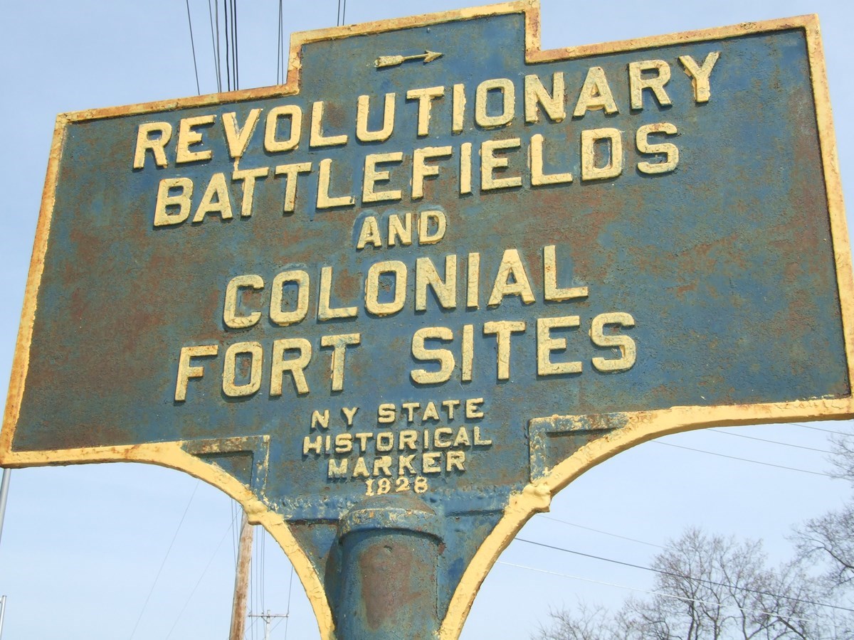 A rusted NYS historic marker. "Revolutionary Battlefields and Colonial Fort Sites"