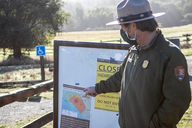A male ranger points to a map of closures at a trailhead.