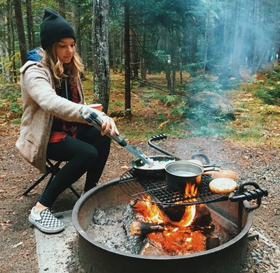 Woman makes breakfast over campground fire ring