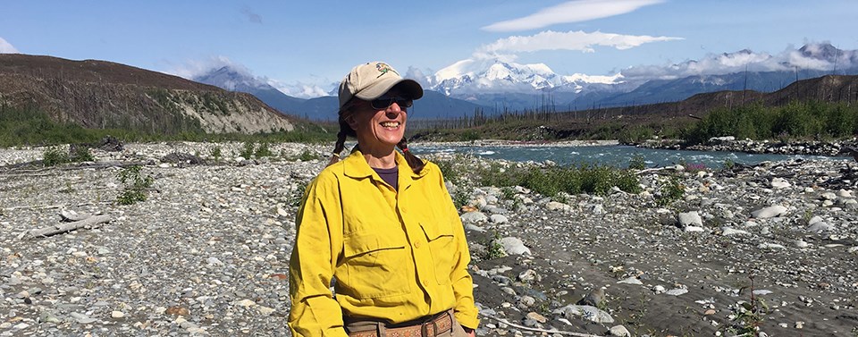 A smiling woman stands on a rocky bar near a waterway.
