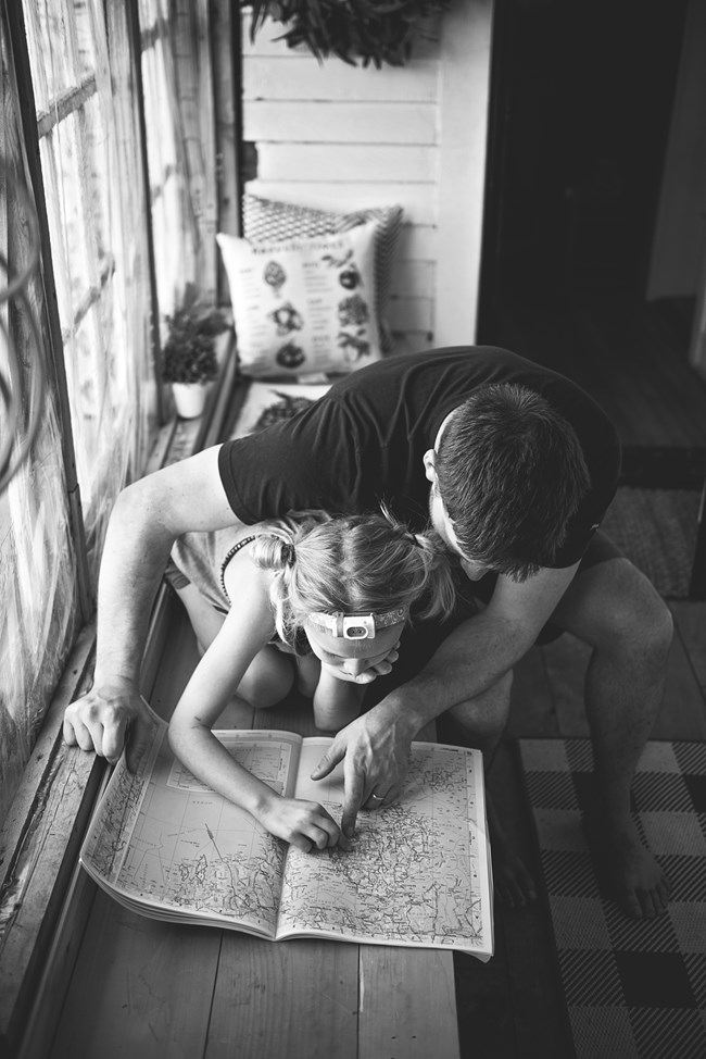 Small girl and her father lean over to examine a trail map closely