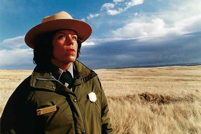 Barbara Sutteer in her NPS uniform standing in front of a field under a cloudy blue sky.