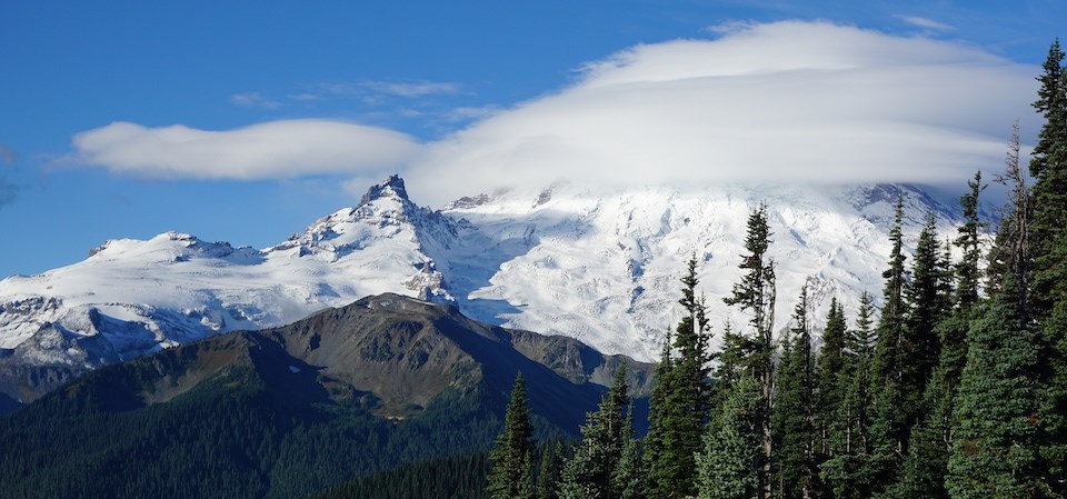 A glaciated mountain with its peak wrapped in clouds against a blue sky.