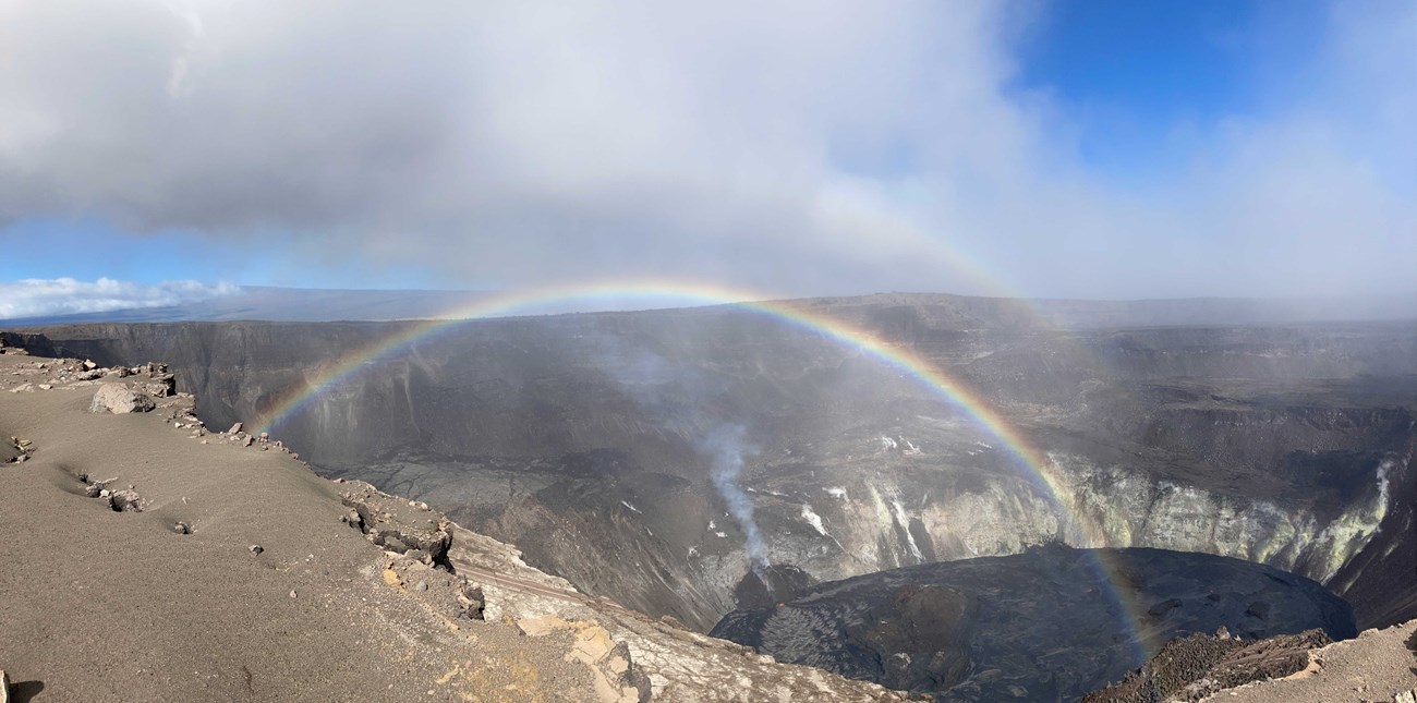 photo of a summit crater with a rainbow and clouds
