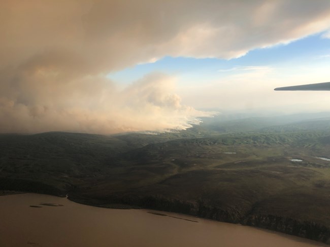 Cultas Creek Fire on July 2, 2021 Image taken from aircraft showing billowing smoke from a forested area in the distance behind a large water body.