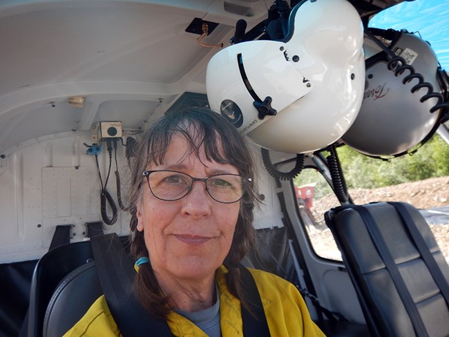 Jennifer Barnes sits in a helicopter with a flight helmet nearby.