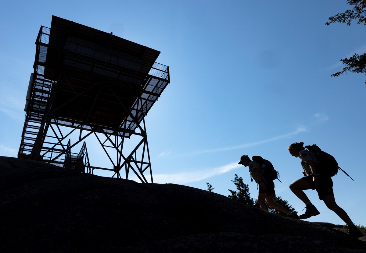 Silhouettes of two hikers approaching a fire tower