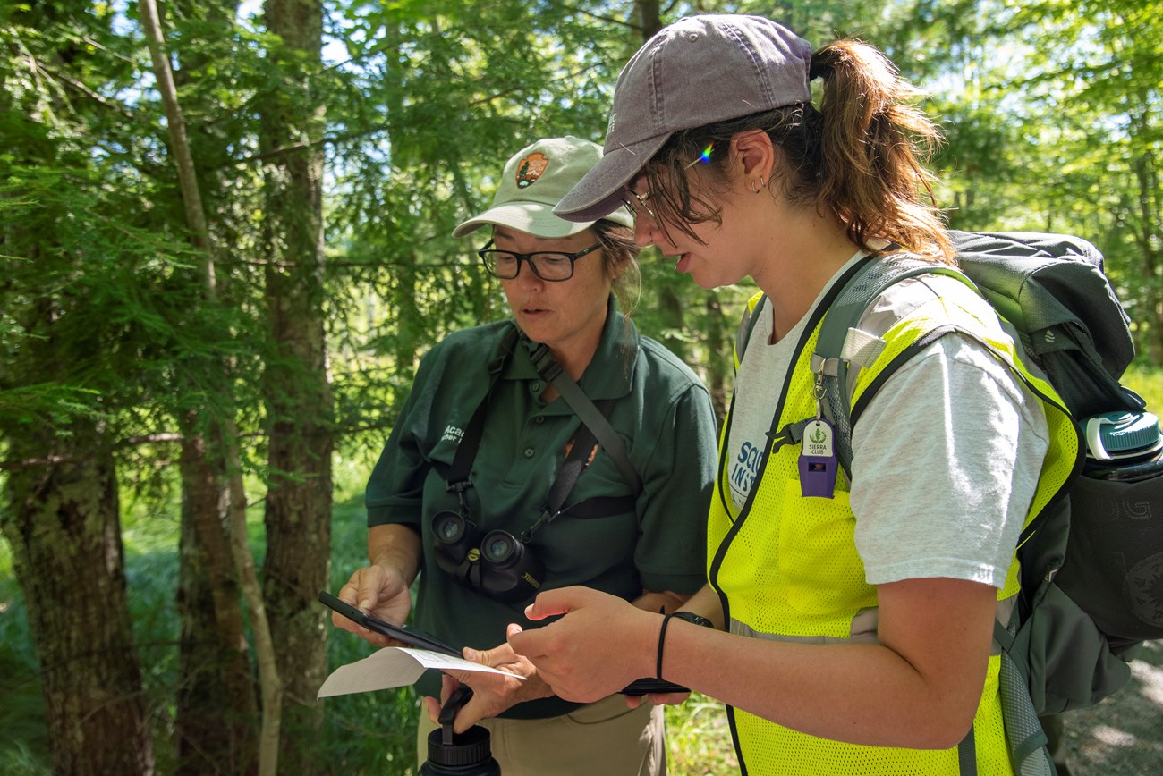 Two women in uniform in an outdoor setting have a conversation while holding electronic devices. Two women in uniform in an outdoor setting have a conversation while holding electronic devices.