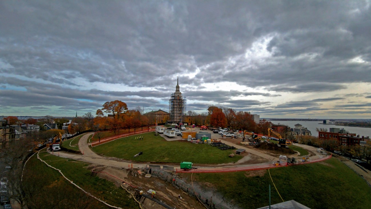 Image of a park under construction with vehicles and a central monument surrounded by scaffolding.