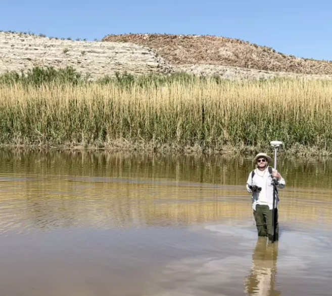 International Volunteer Josh Richards stands in a stream, helping to collect water data.