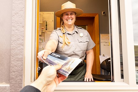1 - Purchase a Park Entrance Pass Online web a park ranger handing a brochure to someone in a vehicle at an entrance station
