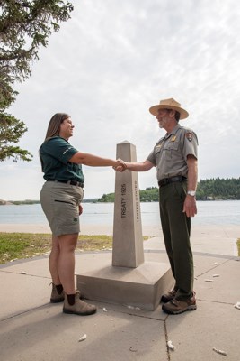 Two people in uniform shake hands near a obelisk.