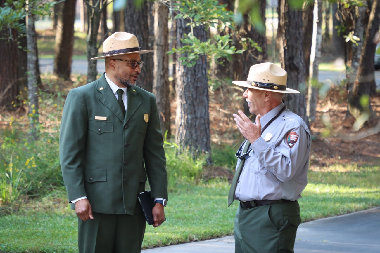 Rangers Hatten and Prokopetz 2 park rangers standing outside talking to each other. One is wearing a formal green jacket. The other is gesturing with his hands.