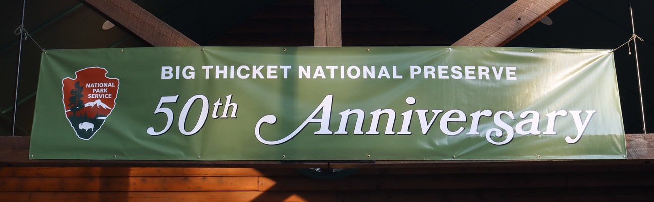banner a large banner hanging from wooden beams that reads: Big Thicket National Preserve 50th Anniversary. The National Park Service arrowhead logo is featured.