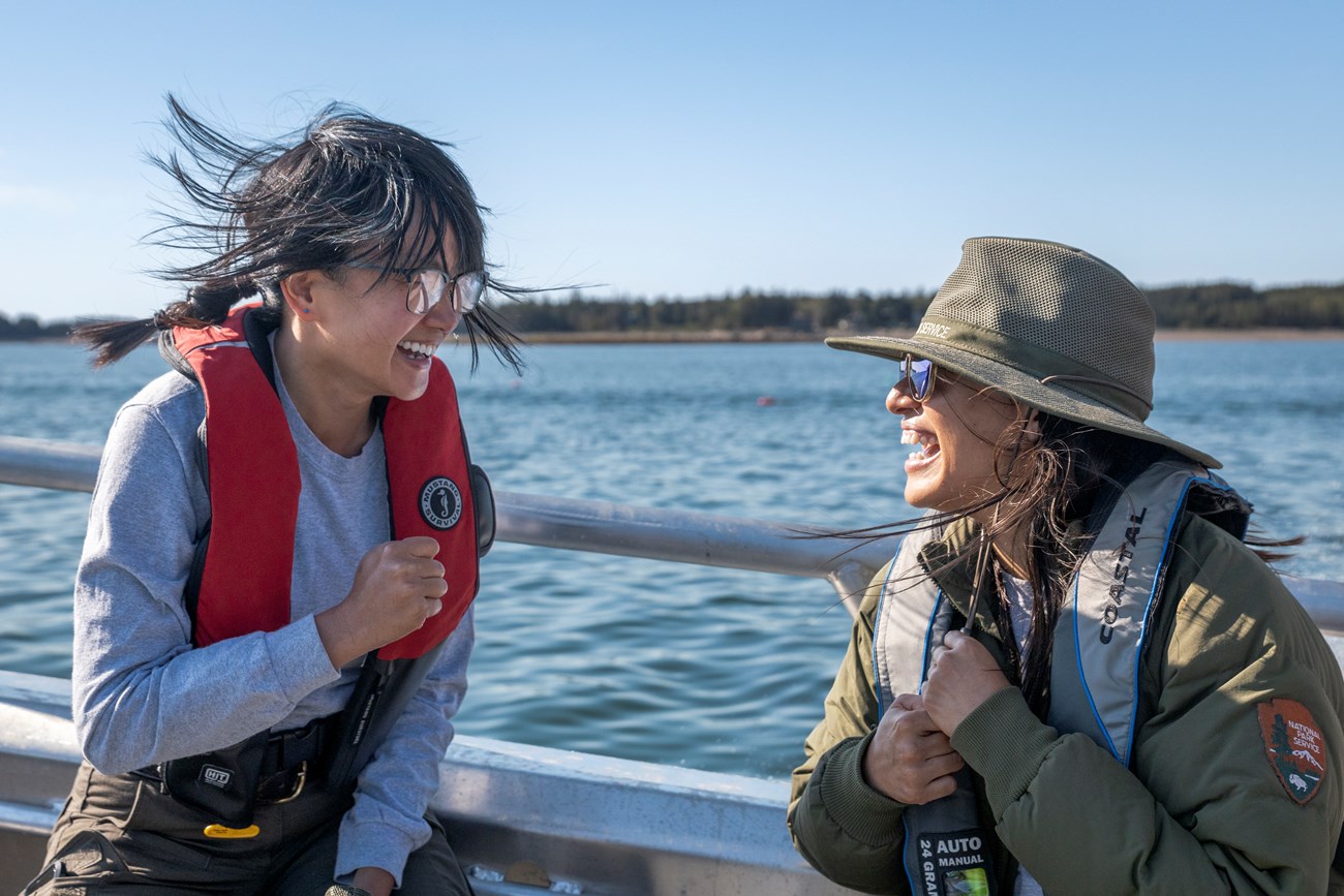 Two park rangers smiling and laughing while on a boat in the ocean.
