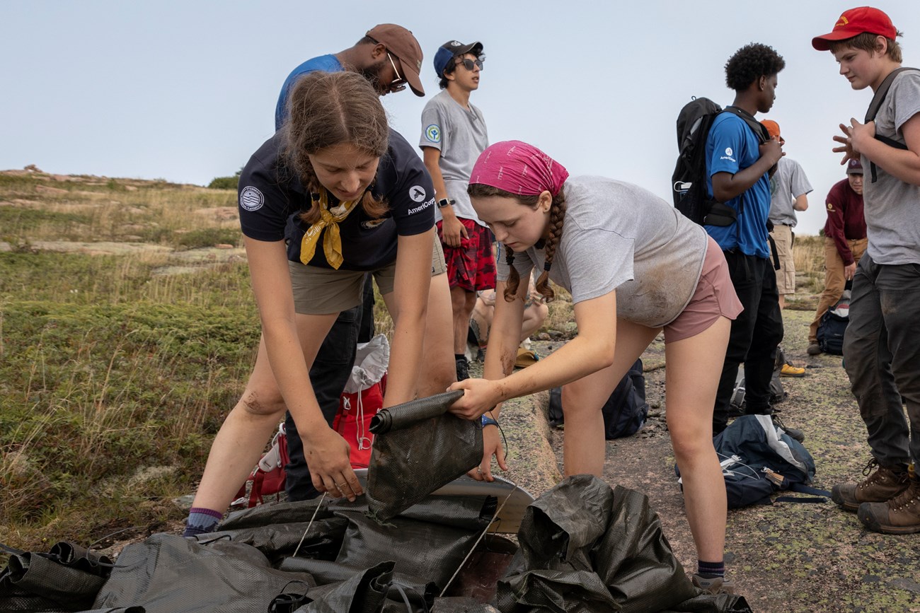 Claire Burnet placing bag of soil with a volunteer onto the restoration area. Two women place a bag of soil into a restoration area on Sargent Mountain.