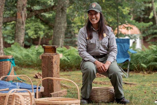 A woman demonstrating the strength of a black ash basket by sitting on it.