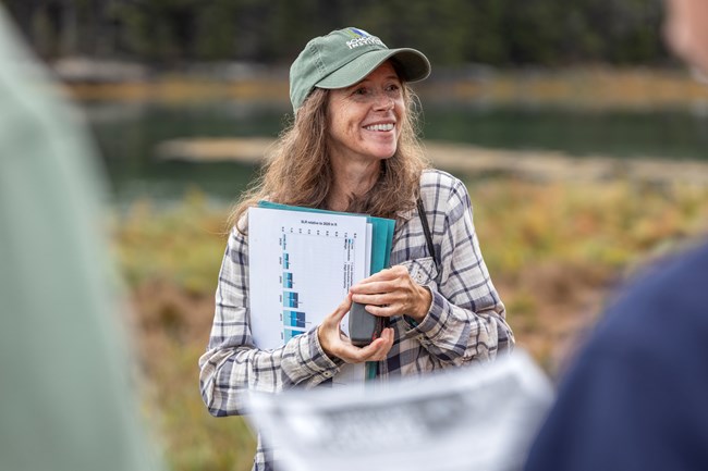 Catherine smiles in front of a crowd while holding a series of scientific papers. Woman smiles in front of a crowd while holding a series of scientific papers.